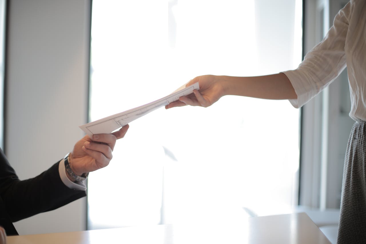 The Art of Drawing Readers In: Your attractive post title goes here Close-up of hands exchanging documents in a business setting indoors.